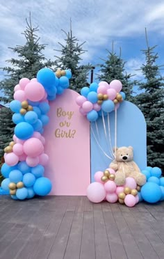 a teddy bear sitting in front of a pink and blue arch with balloons on it