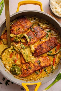 a pan filled with fish and vegetables on top of a white counter next to rice