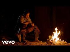 a man sitting in front of a fire with his hands on his knees and looking at something