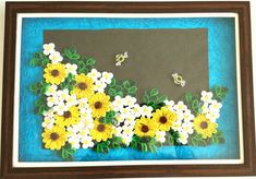 an art project made with paper and flowers on a blue background is displayed in a frame