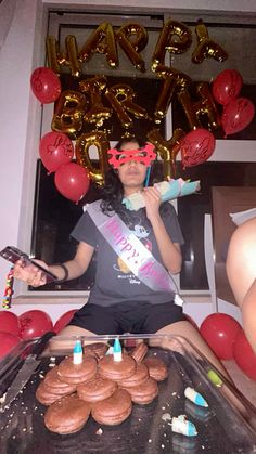 a woman sitting in front of a table with cupcakes and balloons