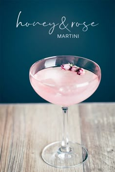 a pink drink in a martini glass on a wooden table with the words honey & rose written above it