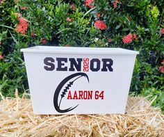 a white cooler with the words senior and aaron 64 on it in front of some flowers