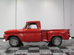 an old red pick up truck parked on a checkered floor