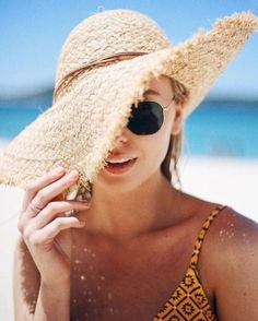 a woman wearing a hat and sunglasses on the beach