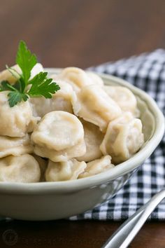 a white bowl filled with dumplings and garnished with green leafy parsley