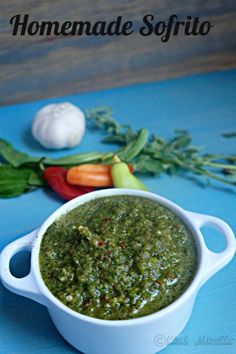 a white bowl filled with pesto next to garlic, peppers and carrots on a blue surface