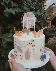 a person holding a cake with animals on it and the number three candles are lit