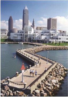 people are walking on the pier in front of some buildings and water with tall buildings behind them