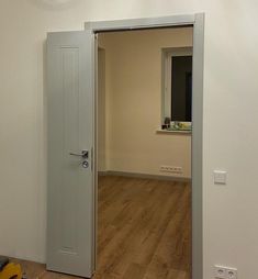 an empty room with hard wood flooring and a white door leading to a window