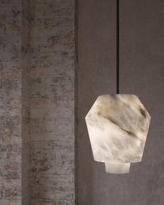 a white marble lamp hanging from a black cord in a room with concrete walls and flooring