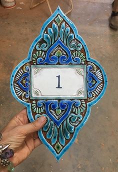 a hand holding up a decorative plaque with the number one on it