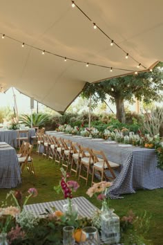 tables and chairs are set up under a tent for an outdoor event with lights strung from the ceiling