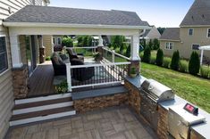 an outdoor kitchen with grill and seating on the back deck in front of a house