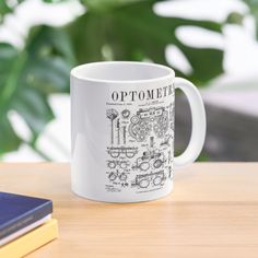 a white coffee mug sitting on top of a wooden table next to a book and plant