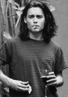 a black and white photo of a man with long hair holding a drink in his hand