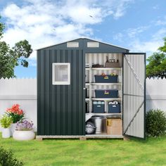 a shed with its doors open in the grass next to a white fence and flowers