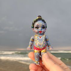 a hand holding a small doll in front of the ocean