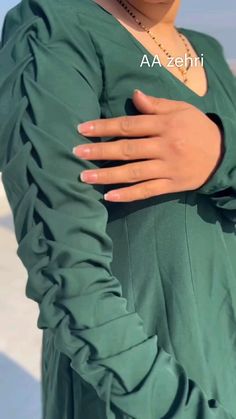 a woman wearing a green dress with her hands on her chest and the words azshi written in arabic