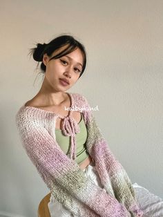 a woman sitting on top of a wooden chair wearing a pink and white knitted sweater