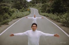 two people standing in the middle of an empty road with their arms spread wide open