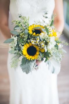 a bride holding a bouquet of sunflowers and greenery