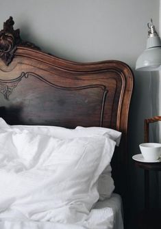 a bed with white linens and a wooden headboard next to a wall lamp