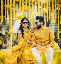 a man and woman sitting on a yellow couch in front of some hanging garlands