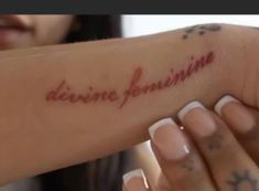 a woman is holding her arm with the word divine feminine written on it in red ink