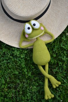 a crocheted frog is laying on the grass wearing a straw hat with eyes