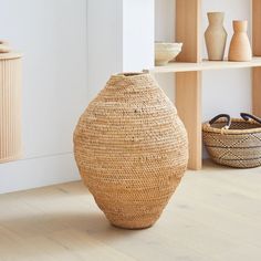 a large woven vase sitting on top of a wooden floor next to baskets and shelves