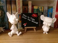 two white figurines sitting on top of a wooden table next to bookshelves