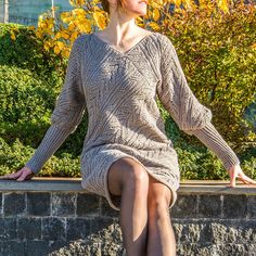 a woman sitting on top of a brick wall wearing a sweater dress and high heels