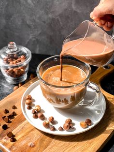 someone pouring milk into a cup on top of a white plate with nuts around it