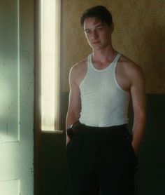 a man standing in front of a window wearing a white tank top and black pants