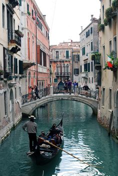 a gondola in the middle of a canal with people standing on it and buildings lining both sides