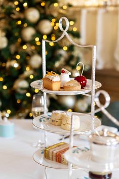 three tiered trays filled with pastries on a table in front of a christmas tree