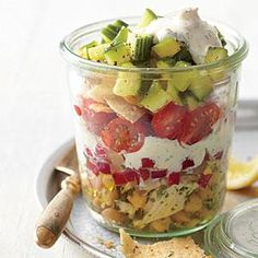 a salad in a glass jar with dressing on the side and lemon wedges next to it