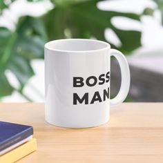 a white coffee mug with the words boss man on it sitting next to a book