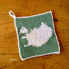 a green and white crocheted pot holder with flowers on it sitting on top of a wooden table