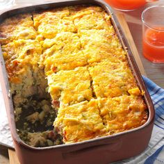 a casserole dish with meat and vegetables in it next to two glasses of orange juice