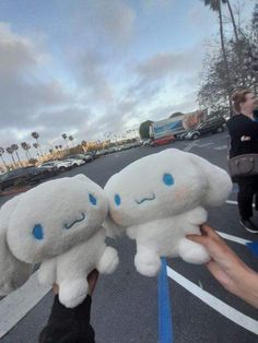 someone holding two stuffed animals in the middle of a parking lot with cars behind them