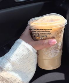 a woman's hand holding a cup of coffee in the passenger seat of a car