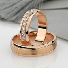 two gold wedding rings with diamonds on them sitting on a white surface next to each other