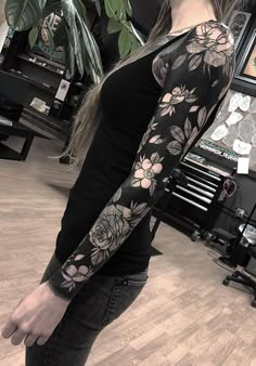 a woman with long hair wearing a black shirt and flower sleeve tattoo on her arm