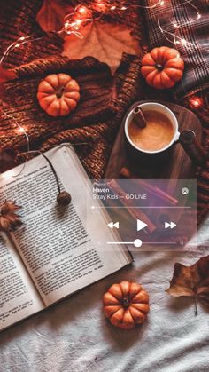 an open book sitting on top of a bed next to a cup of coffee and pumpkins