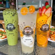 three different types of drinks sitting on a table with plates of food in the background