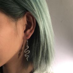 a woman with green hair wearing silver earrings