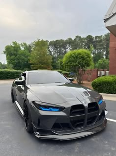 a grey sports car parked in a parking lot next to a building with trees and bushes behind it