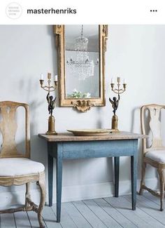 two chairs and a table with a mirror on the wall above it, in front of a chandelier